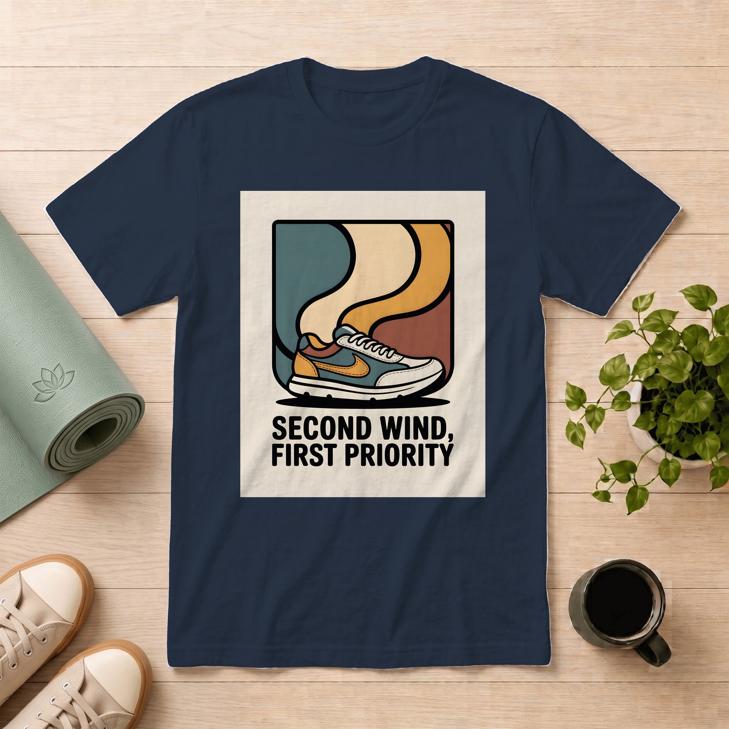 A navy blue graphic t-shirt laid flat on a light wood surface, surrounded by lifestyle props including a yoga mat, sneakers, a potted plant, and a coffee mug. The t-shirt features a retro sneaker illustration with the text 'SECOND WIND, FIRST PRIORITY'.